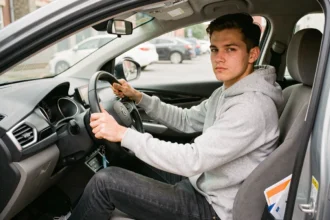 Jeune conducteur assis au volant d'une voiture de 7 CV avec un dossier d'assurance auto visible