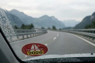 Vignette autoroutière suisse 2026 collée sur un pare-brise avec autoroute alpine en arrière-plan