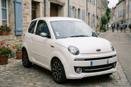 Petite voiture sans permis blanche garée dans une rue de ville française avec des façades en pierre en arrière-plan
